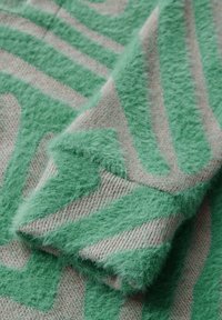 Tissu vert duveteux avec un motif texturé, présentant des rayures ondulées sur un fond beige. Texture douce et chaude avec un aspect distinct.