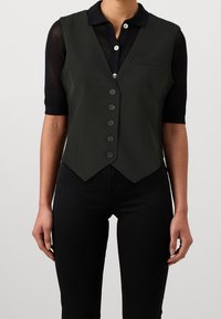 Svart ärmlös väst med en figurnära design, gjord av ett slätt material. Har en spetsig nederkant, knäppning framtill och en liten bröstficka.