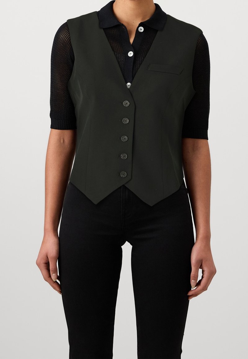 Svart ärmlös väst med en figurnära design, gjord av ett slätt material. Har en spetsig nederkant, knäppning framtill och en liten bröstficka.