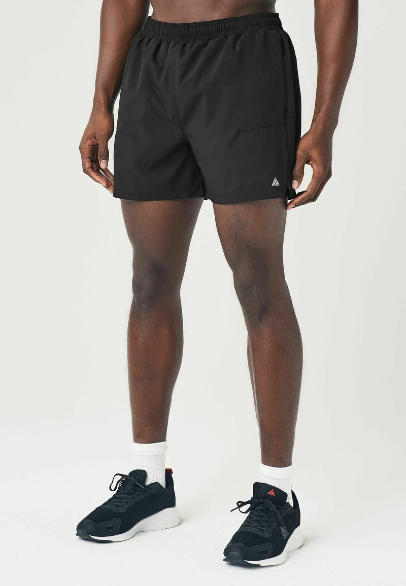 Sorte atletiske shorts med elastisk talje, sidelomme og diskret logo. Bæres med sorte sneakers og hvide ankelstrømper.