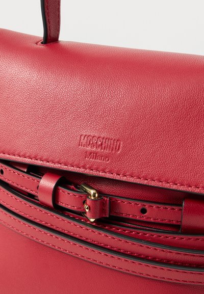 Κόκκινη δερμάτινη τσάντα Moschino Milano με λουρί και αγκράφα και ορατές ραφές στην υφασμάτινη επιφάνειά της.