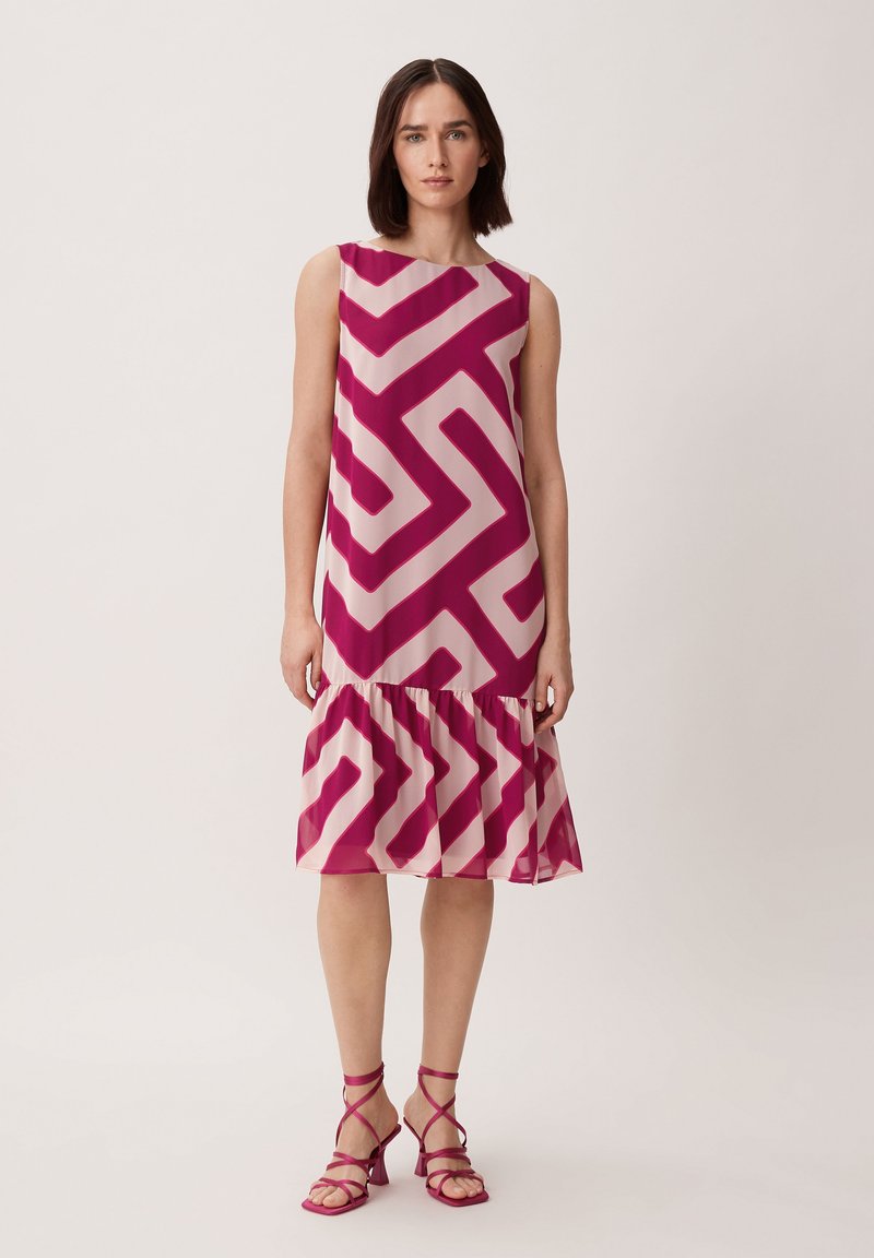 Kleid aus transparenter Stoff mit einem geometrischen Zickzackmuster in Rosa und Creme, mit einem ausgestellten Saum. Kombiniert mit passenden Sandalen mit Riemchen.