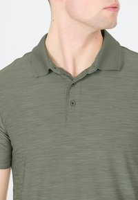 Oliven grøn polo t-shirt i et tekstureret stof, der har en krave, tre knaplukninger og korte ærmer, med subtile horisontale linjer.