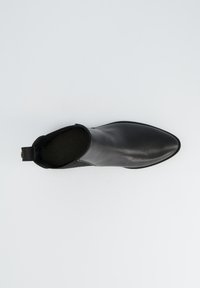 Bottine en cuir noir avec un bout pointu et un panneau arrière texturé. Dispose d'une languette à l'arrière pour un enfilage facile.