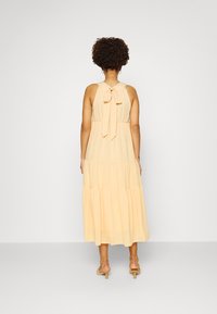 Vestido maxi em amarelo pálido, feito de tecido leve. Apresenta um decote halter amarrado, design em camadas e uma textura subtil. Estilizado com sapatilhas de tiras.
