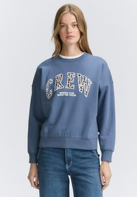 Felpa a girocollo realizzata in morbido cotone blu, con una bold grafica "CREW" contornata da una stampa leopardata e polsini a costine. Vestibilità casual.