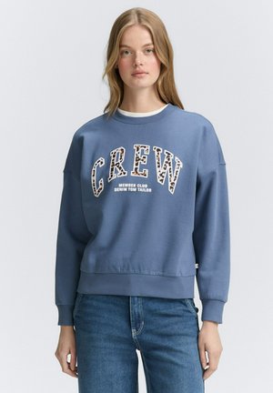 Felpa a girocollo realizzata in morbido cotone blu, con una bold grafica "CREW" contornata da una stampa leopardata e polsini a costine. Vestibilità casual.