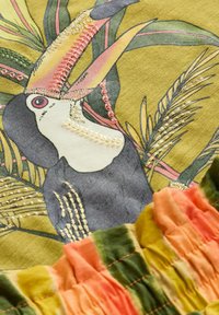 Embroidered fabric featuring a toucan surrounded by colorful leaves. Patterns include pink, green, and orange with textured stitching details.