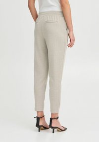 Lys grå herringbone joggebukser med elastisk liv og to baklommer, kombinert med svarte hælsandaler.