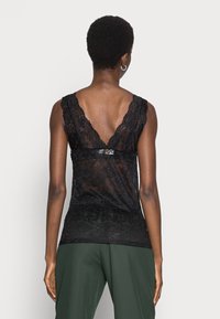 Top in pizzo nero con design a V sulla schiena, intricati motivi floreali e ampia rifinitura in pizzo sulle spalle. Texture morbida, forma aderente.