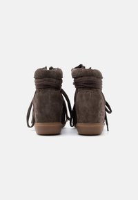 Ζευγάρι από καφέ σουέντ μπότες αστραγάλου με χοντρές καφέ κορδόνια και ανοιχτό καφέ λαστιχένιες σόλες, εμφανιζόμενες από πίσω σε λευκό φόντο.