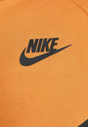 Sudadera naranja de Nike con un logo negro, hecha de una tela texturizada con un patrón de costilla. Incluye un escote redondeado y detalles de costura.