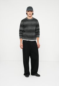 Γκρι πλεκτό πουλόβερ με οριζόντιες ρίγες, μαύρο παντελόνι σε φαρδιά γραμμή και σκούρο καπέλο. Υφασμάτινη υφή, χαλαρή εφαρμογή και μονοχρωμία.