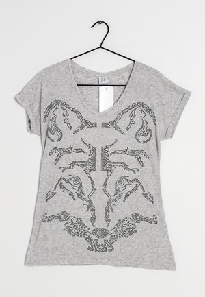 Jasnoszara koszulka z dekoltem w serek na czarnym wieszaku z podwiniętymi rękawami i czarnym wzorem ćwieków przypominającym tygrysią twarz z przodu.