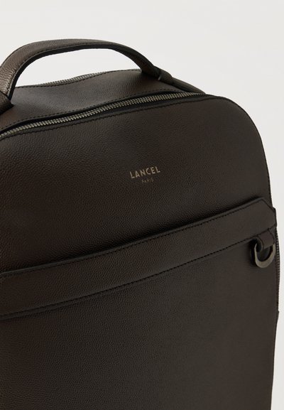 Тъмен кафяв кожен раница Lancel Paris с горна дръжка, преден джоб с цип и метален пръстен като детайл отстрани.