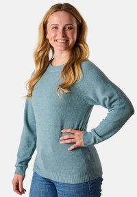 Hellblaues Strickpullover mit weicher Textur, Rundhalsausschnitt und gerippten Bündchen und Saum. Das Modell trägt ihn mit blauen Jeans, was die Passform und den Stil zur Geltung bringt.