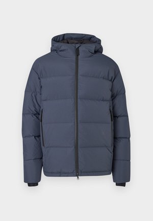 Tumši zilā puffer jaka ar kapuci, ar garu rāvējslēdzēju, divām sānu kabatām un melnu apdari uz piedurknēm. Gluda, matēta auduma tekstūra.