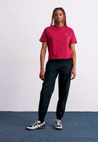 Kurzärmliges, kurzes burgunder T-Shirt mit rundem Ausschnitt und einem Logo; schwarze, schmal zulaufende Jogginghosen mit elastischen Bündchen; getragen mit schwarz-weißen Sneakers.