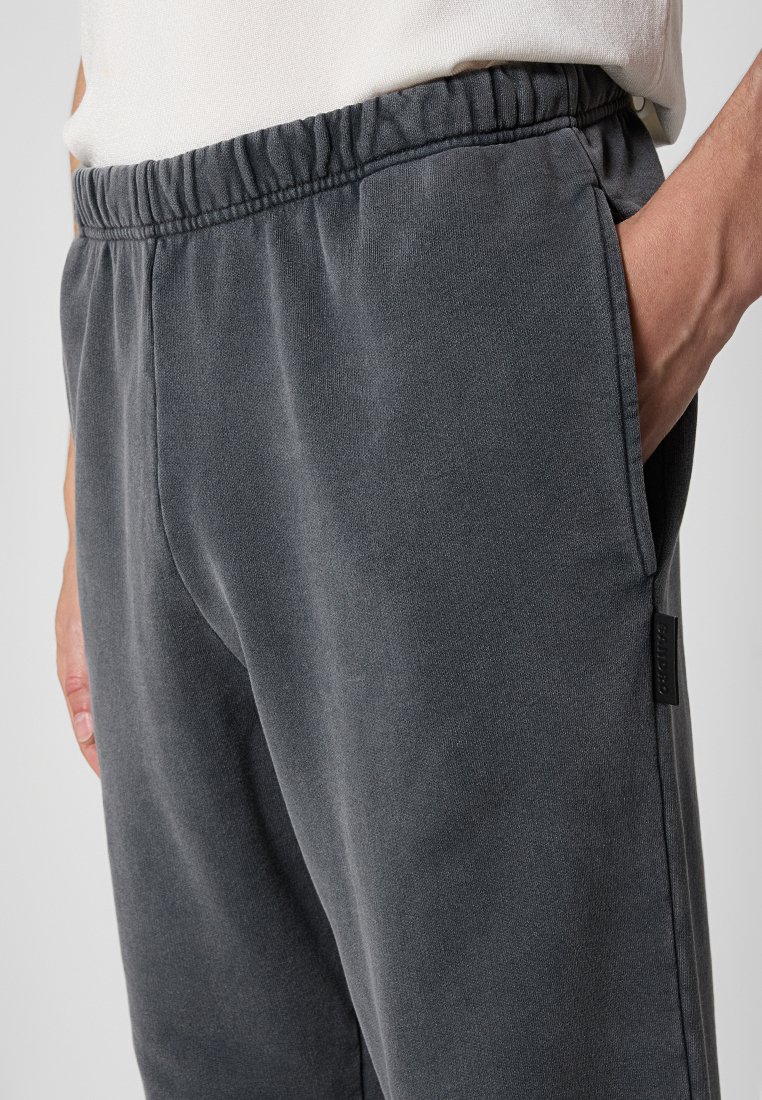 Pantalones de chándal grises con cinturilla elástica, bolsillos laterales y un acabado texturizado. Presenta una pequeña etiqueta de la marca en el lado izquierdo.