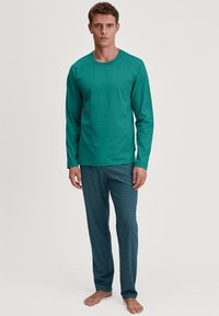 Turquoise lange mouwen shirt gecombineerd met gestreepte blauwe pyjamabroek met golvende patronen. Het materiaal lijkt zacht en comfortabel te zijn.