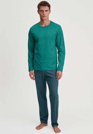 Turquoise lange mouwen shirt gecombineerd met gestreepte blauwe pyjamabroek met golvende patronen. Het materiaal lijkt zacht en comfortabel te zijn.