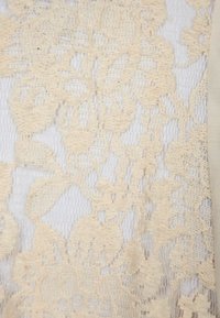 Beige spets tyg med blommönster som ligger ovanpå en vit bakgrund. Intrikat struktur och delikata detaljer är framträdande.