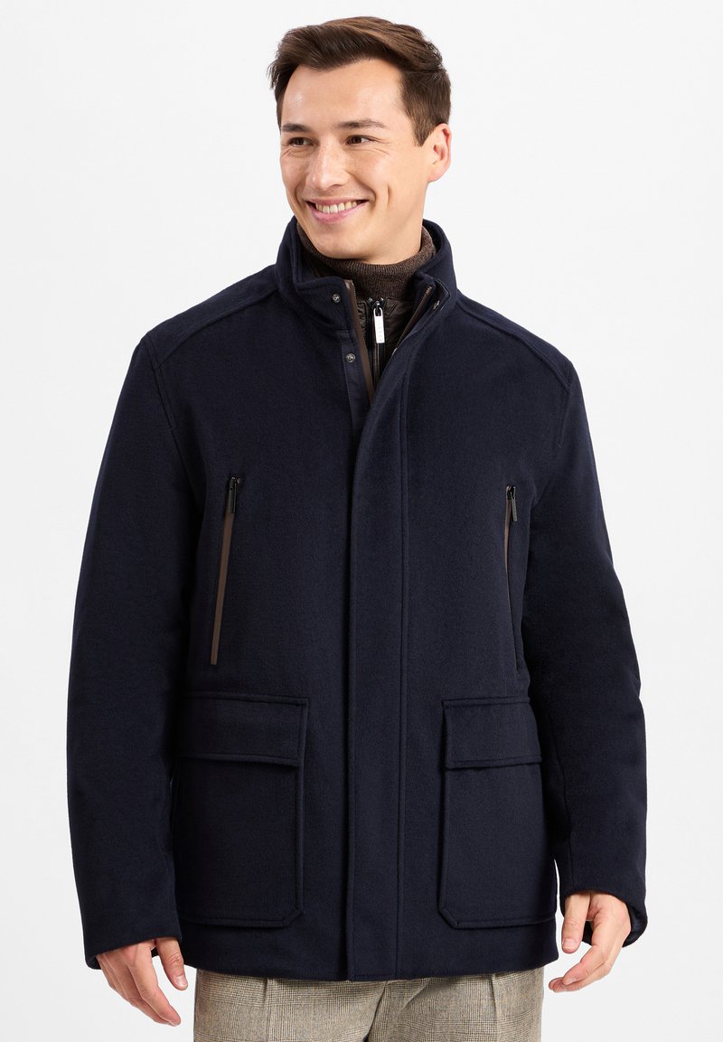 Marineblauer Wollmischungsmantel mit hohem Kragen, Reißverschlusstaschen und aufgesetzten Taschen auf der Vorderseite. Glatte Textur mit taillierter Passform.