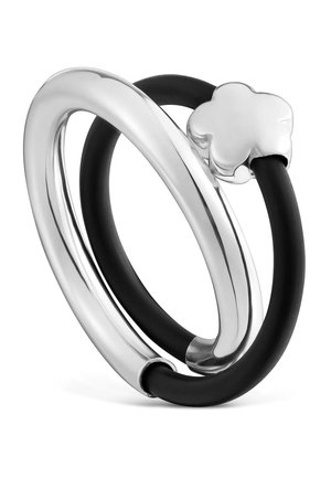 Anillos entrelazados de plata y negro, uno ovalado y liso en plata, el otro negro con un detalle de trébol de cuatro hojas en plata.