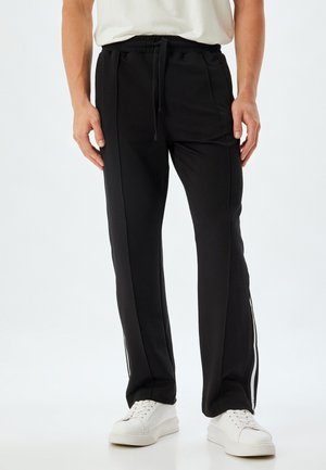 Pantalones deportivos negros con cintura elástica ajustable, bolsillos laterales y rayas blancas contrastantes a lo largo de las costuras exteriores. Tejido suave, corte ajustado.