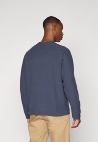 Mørkeblå sweatshirt med lange ærmer, ribbede manchetter og rund hals. Blødt, struktureret stof, der har en afslappet pasform og et enkelt design.