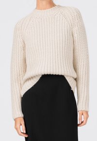 Grovstickad tröja i off-white med ribbat mönster, rund halsringning och sidsprund, parat med en svart kjol. Mjuk, tjockt material.