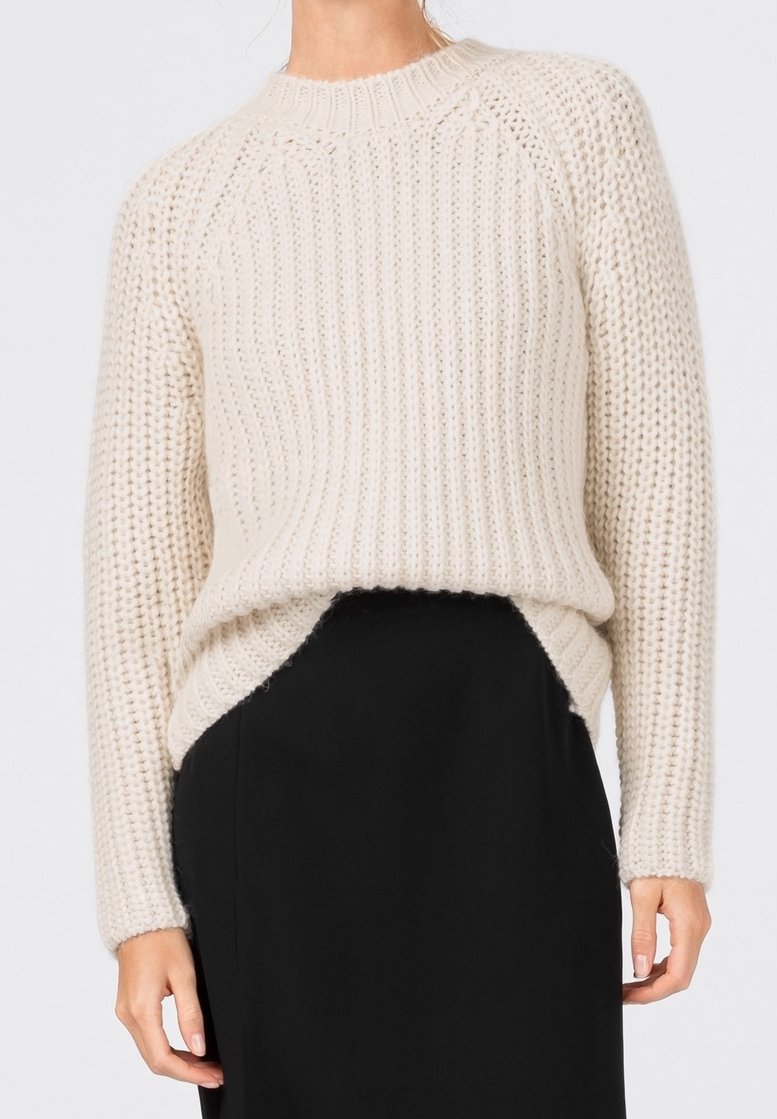 Grovstickad tröja i off-white med ribbat mönster, rund halsringning och sidsprund, parat med en svart kjol. Mjuk, tjockt material.