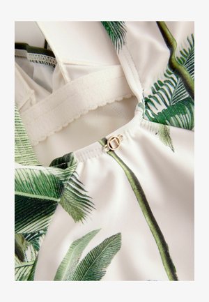 Tropisch-gepatenteerde stof met groene palmbladeren op een witte achtergrond. Bevat een klein gouden cirkelvormig sluitingdetail bij de hals.