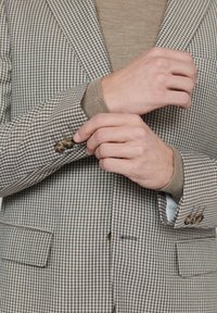 Brun och beige rutmönstrad blazer med en strukturerad passform, utrustad med två brassknappar vid ärmslutet och en bröstficka.