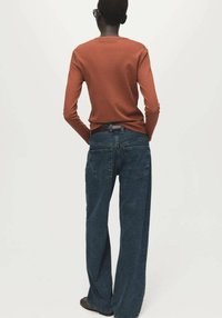 Dolga majica z dolgimi rokavi rjave rjave barve in široke temno modre kavbojke. Majica je oprijeta, kavbojke pa imajo široke hlačnice in dva zadnja žepa.