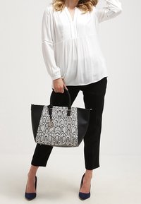 Czarno-biała torebka z wzorem wężowej skóry o usztywnionym kształcie, czarne uchwyty i złote okucia, zestawiona z luźnym białym topem i czarnymi spodniami.