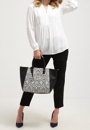 Czarno-biała torebka z wzorem wężowej skóry o usztywnionym kształcie, czarne uchwyty i złote okucia, zestawiona z luźnym białym topem i czarnymi spodniami.