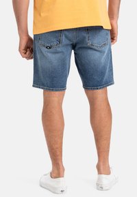 Pantalones cortos de mezclilla en azul desvaído, con corte recto, doble bolsillo trasero y acabado dobladillo. Llevados con zapatillas blancas.