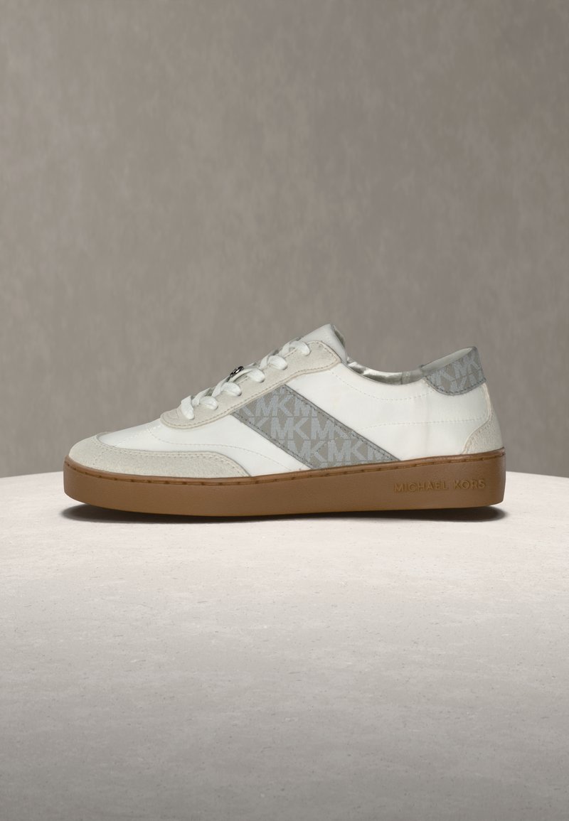 Baskets blanches avec motif logo MK gris, en suède et cuir, semelle en caoutchouc plate, fermeture à lacets et branding discret sur le côté.