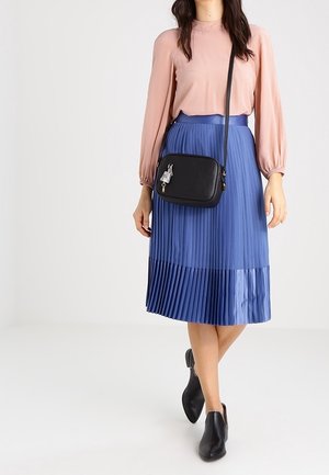 Black leather crossbody bag with a textured finish, featuring a silver charm accent and adjustable strap, paired with a pink blouse and blue pleated skirt.