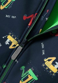 Zbliżenie na zamek błyskawiczny granatowej kurtki z zielonym wykończeniem oraz nadrukami pojazdów budowlanych, w tym żółtej koparki z białym królikiem i napisem "Strefa Robót".