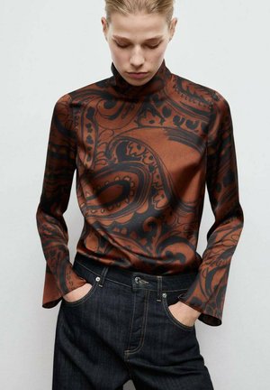 Top de manga larga con estampado marrón y cuello alto, con diseños negros en espiral. Combinado con pantalones de mezclilla oscuros. Textura suave.