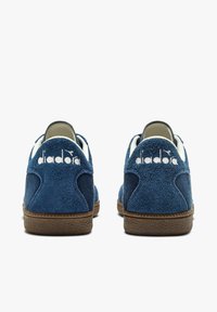 Sneakers in camoscio blu navy con suola in gomma marrone testurizzata e logo bianco sul tallone, con accenti bianchi a contrasto.