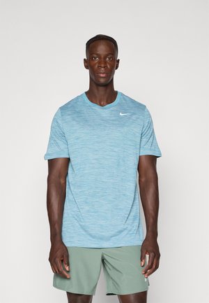 Lyseblå treningst-skjorte med teksturert mønster og rund hals, med en liten hvit Nike-logo øverst til venstre.