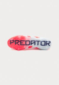 Suela de botas de fútbol roja y blanca con "PREDATOR" en marino. Presenta una superficie texturizada y tacos salientes para mayor tracción.