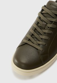 Oliwkowe skórzane sneakersy o fakturowanej powierzchni, zaokrąglonym nosku i dopasowanych sznurowadłach. Posiadają kremową gumową podeszwę oraz minimalne detale szwów.