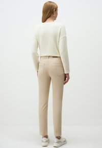 Pantalons beiges ajustés avec une taille mi-haute, poches arrière, associés à un pull en maille texturée crème et des baskets blanches. Design simple et épuré.