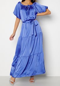 Robe maxi bleu satinée avec design à volants, encolure décolletée et taille ajustable par un lien. Comprend des manches courtes et un tissu fluide.