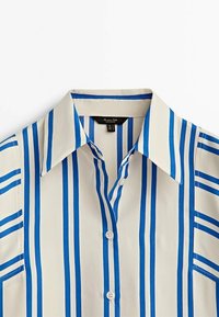 Camicia bianca con bottoni, a righe verticali larghe blu e colletto a punta, esposta flat su uno sfondo bianco.
