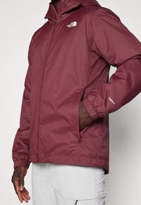 Bordowa wodoodporna kurtka z kapturem, elastycznymi mankietami i bocznymi kieszeniami. Posiada odblaskowe akcenty i zabezpieczony zamek z przodu.